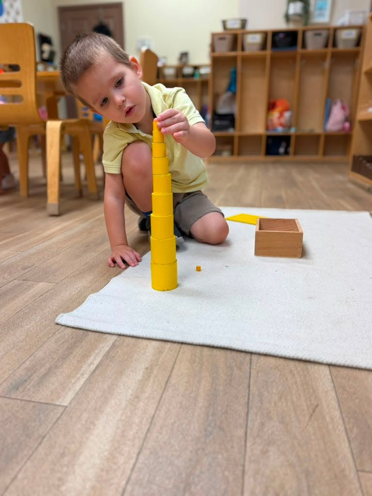 Child stacking yellow cylinders on a mat in a classroom