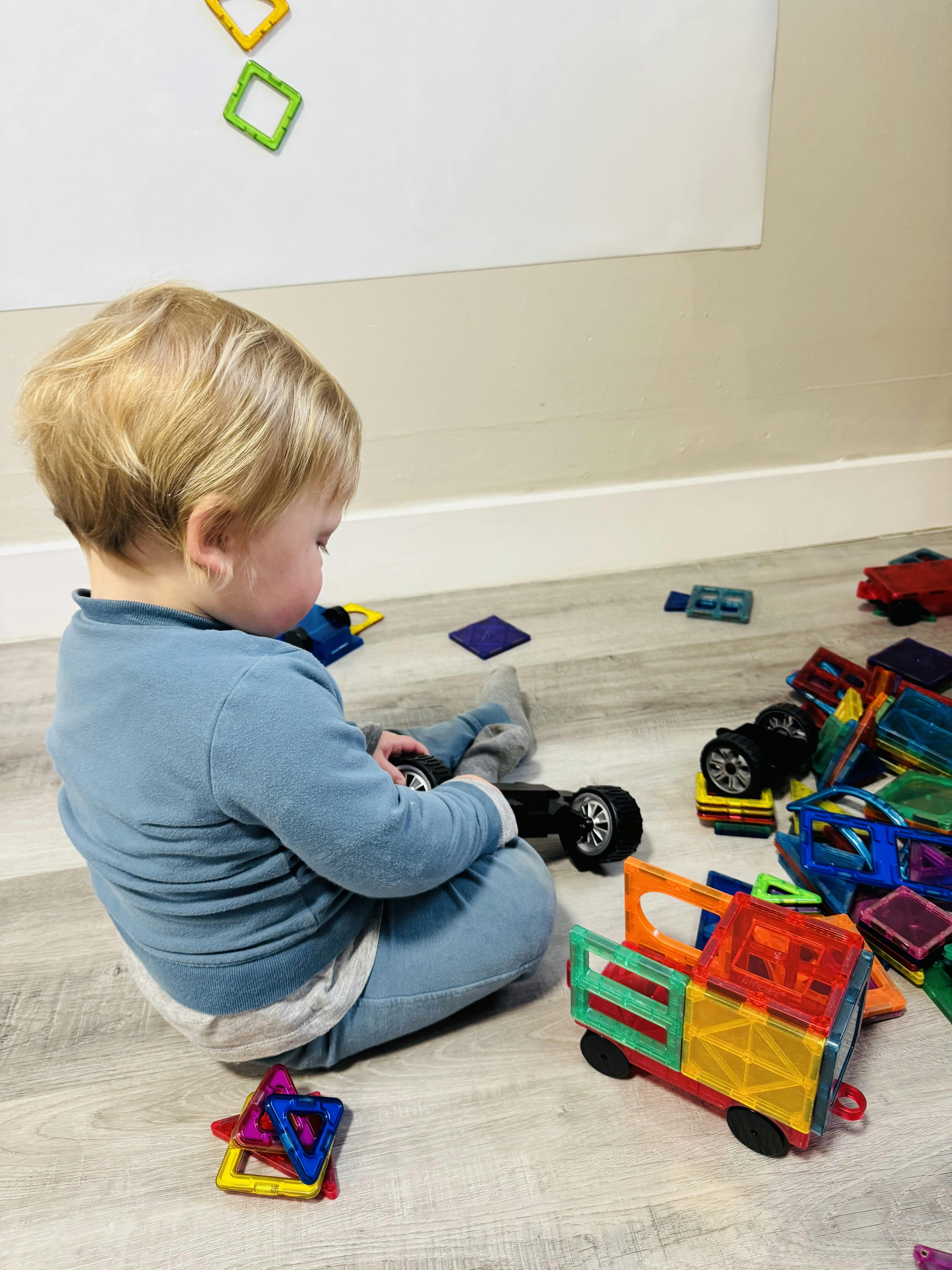 Child playing with magnetic tiles and toy car on the floor