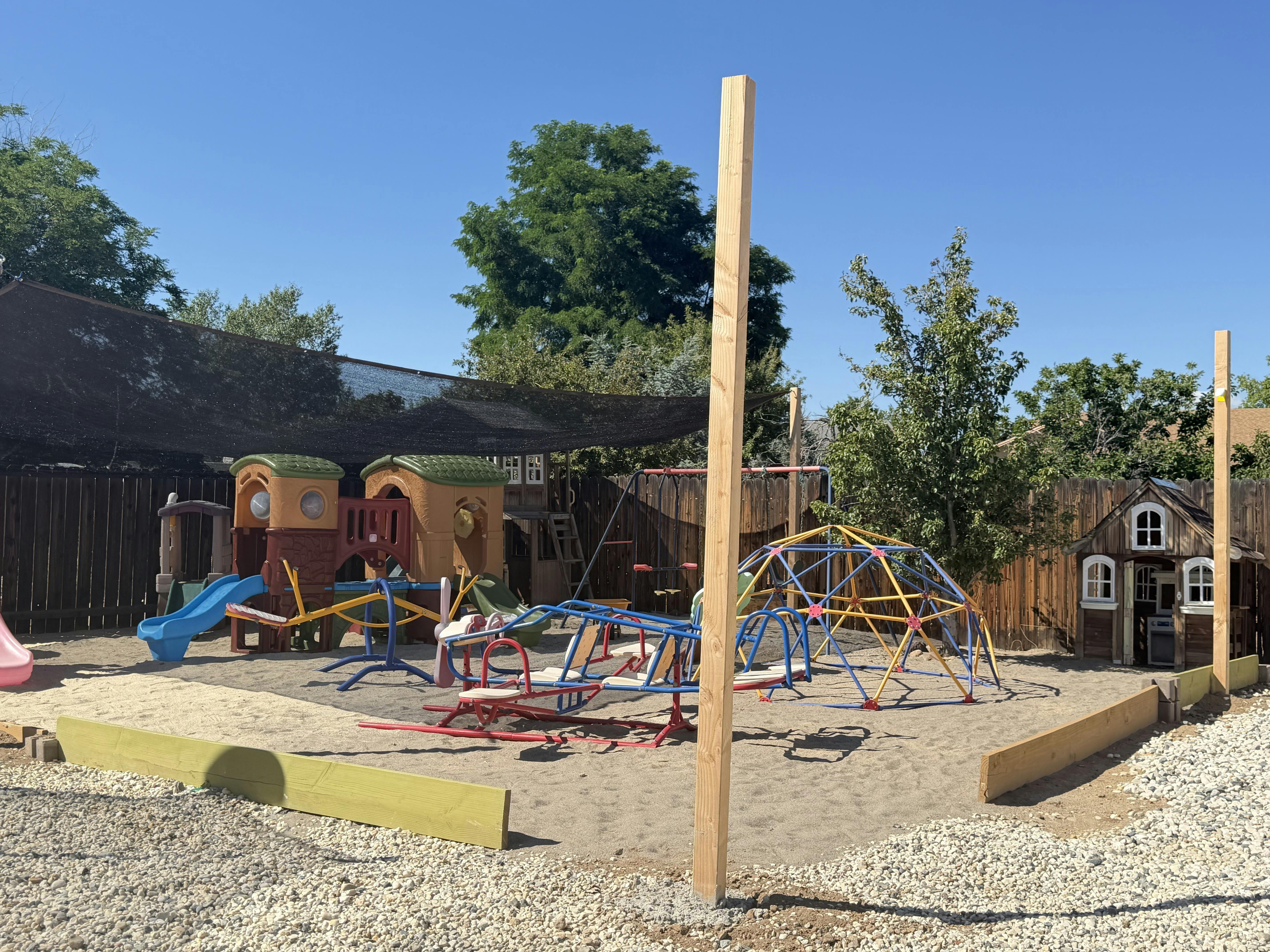 Playground equipment including a slide, climbing dome, and seesaw in a sand area