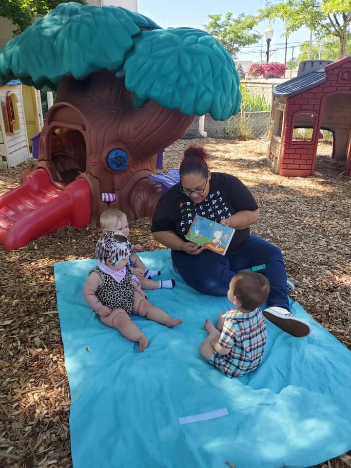 Person reading a book to three children on a blue blanket outdoors