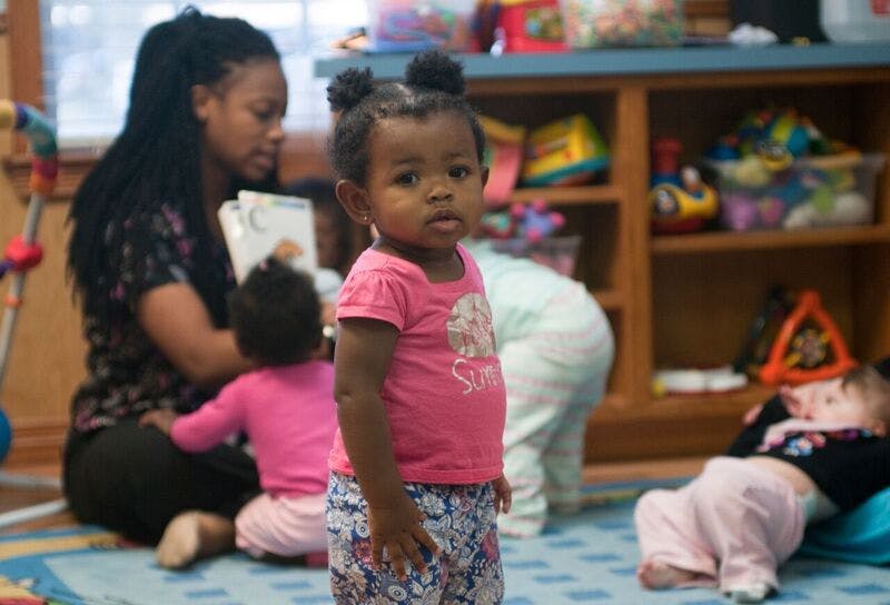 Child standing in foreground, person reading to child in background