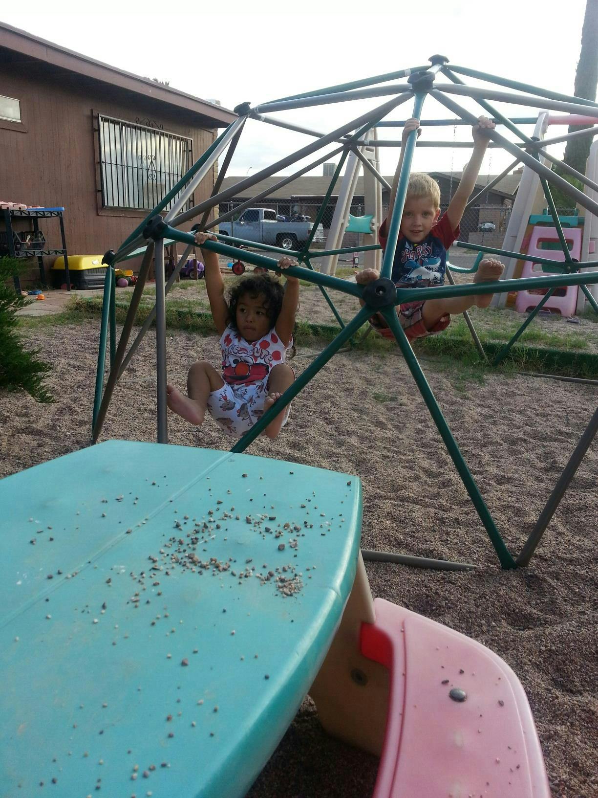 Two children climbing on a geodesic dome in a sandy area