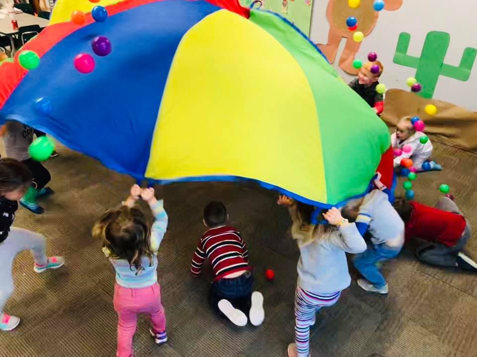 Children playing with a colorful parachute and small balls