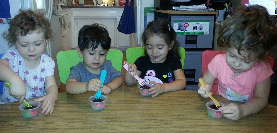 Four children sitting at a table with small cups and spoons
