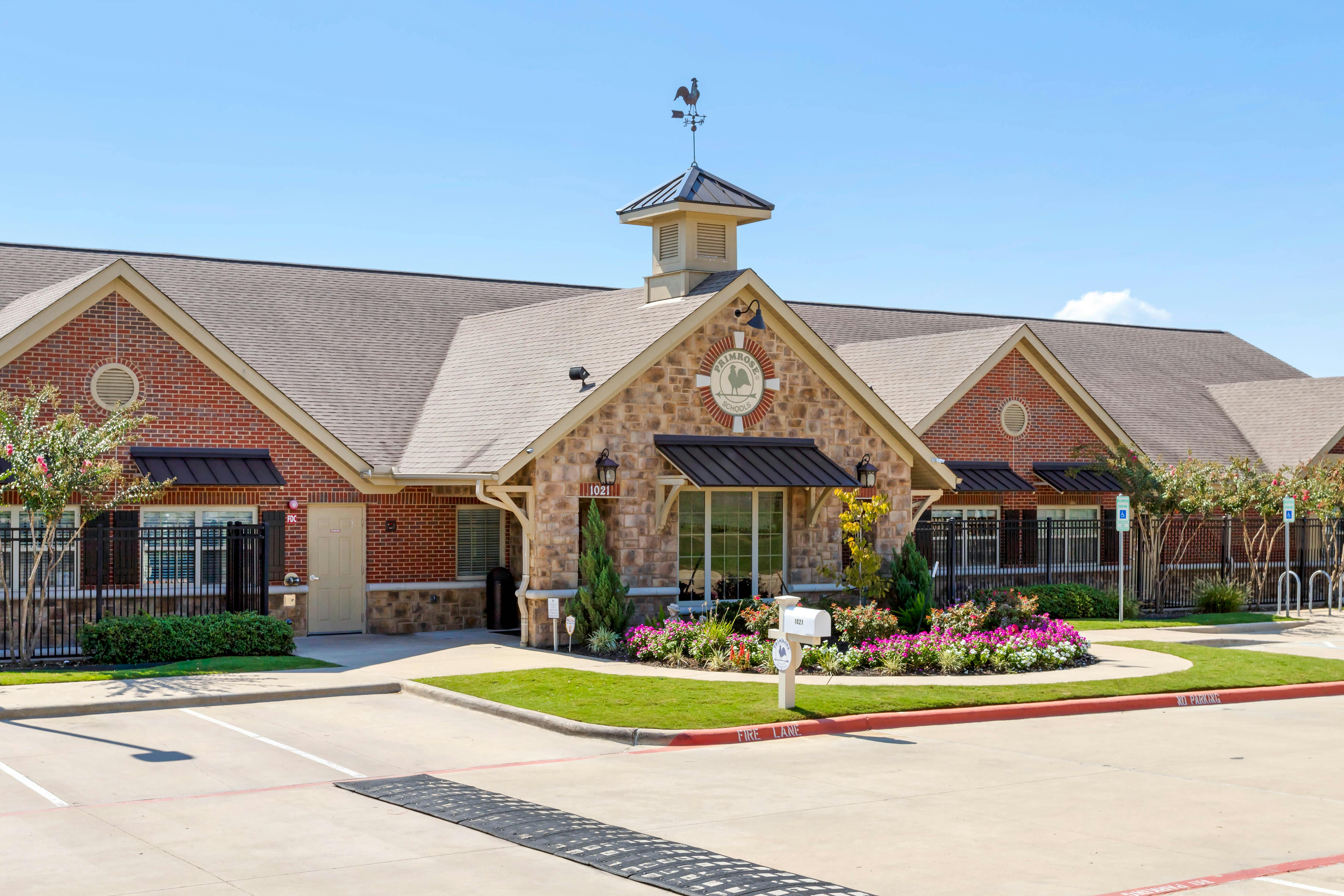 Exterior of a brick and stone building with a weather vane and Primrose Schools logo