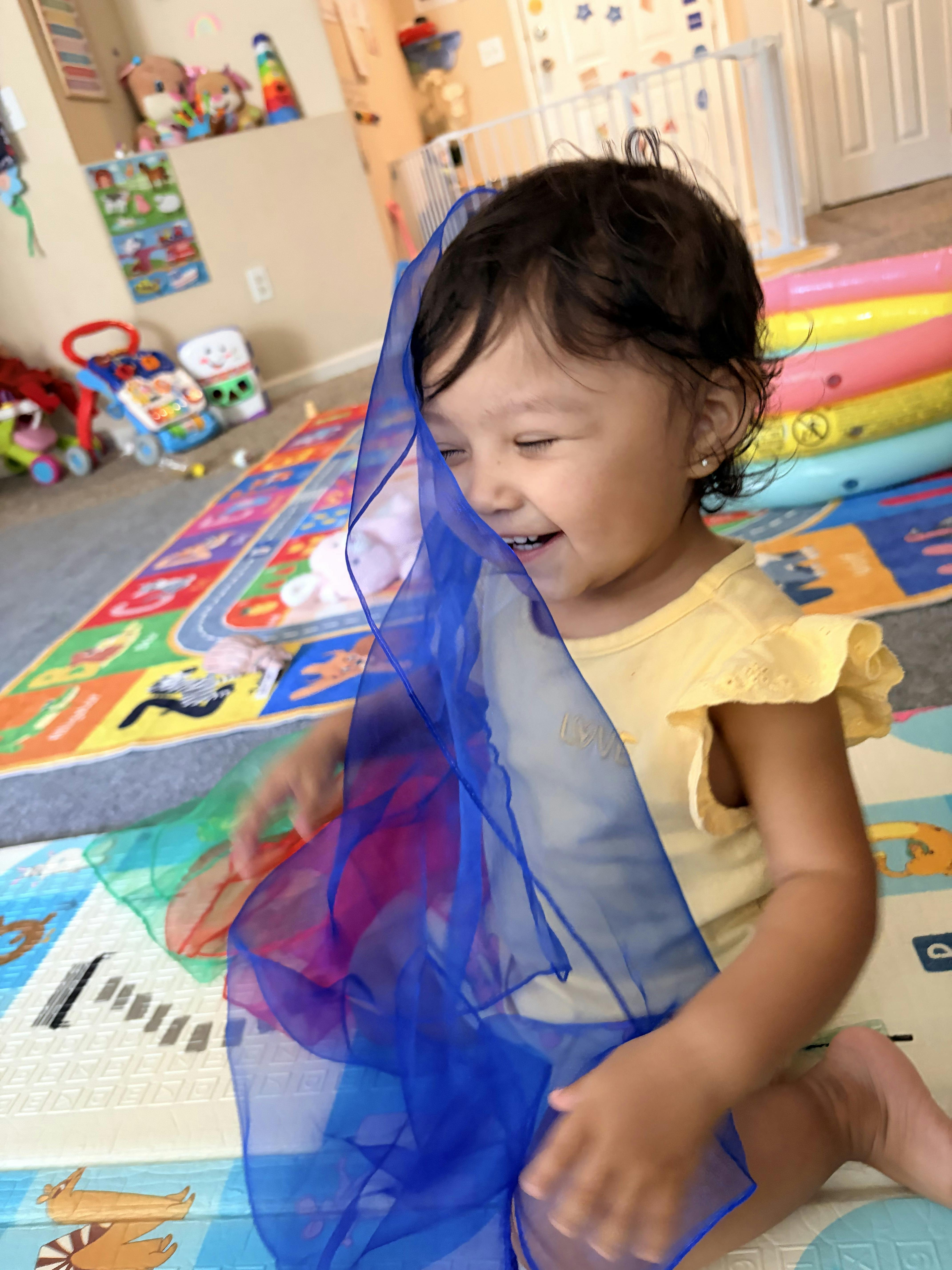 A child playing with a blue sheer fabric on a colorful play mat