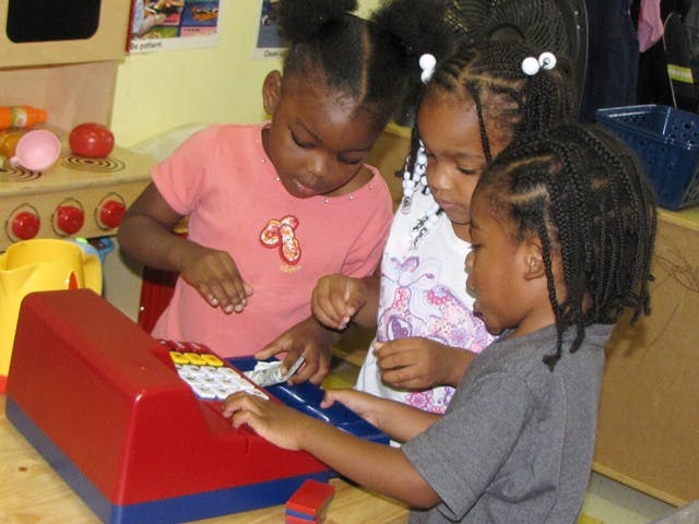Three children playing with a toy cash register