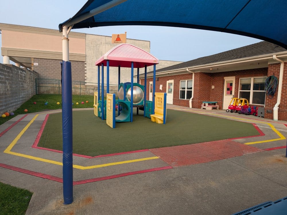 Playground with colorful play equipment in a fenced-in area next to a brick building