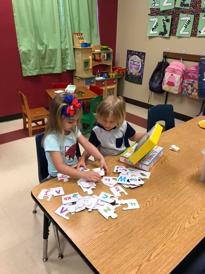Two children playing with letter puzzles at a table