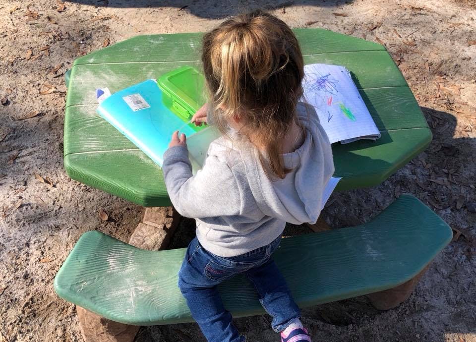 Child sitting at a green picnic table with an open binder and closed notebook
