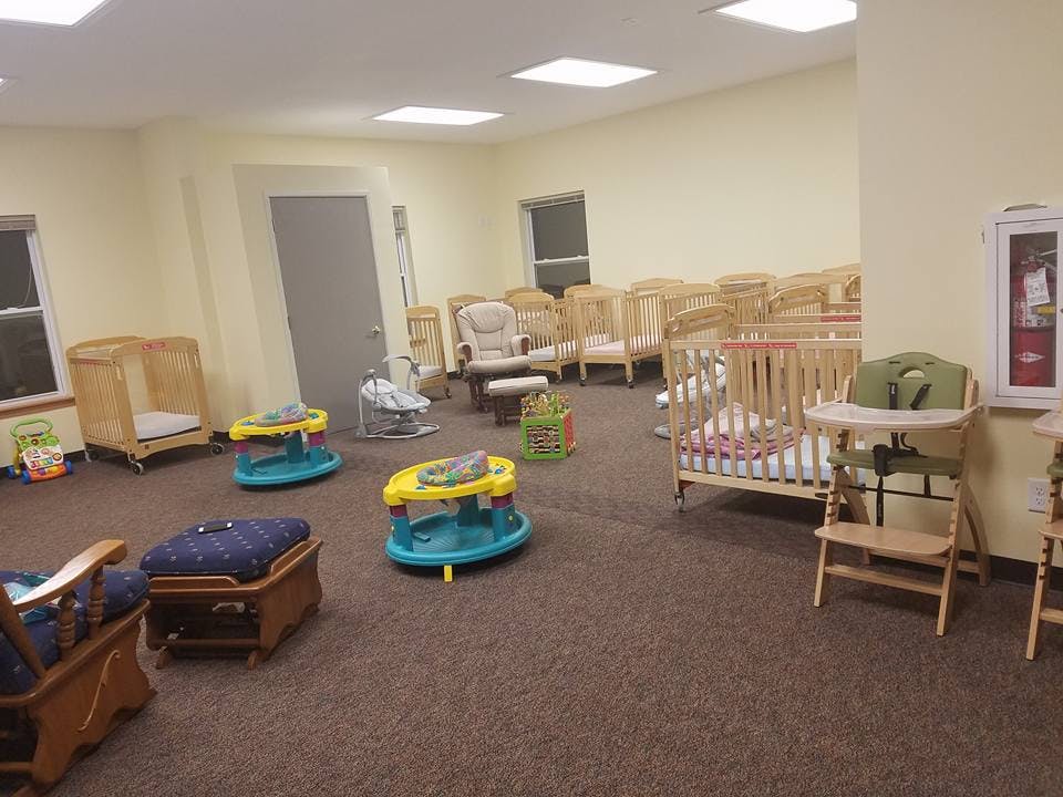 Room with multiple cribs, high chairs, and baby walkers