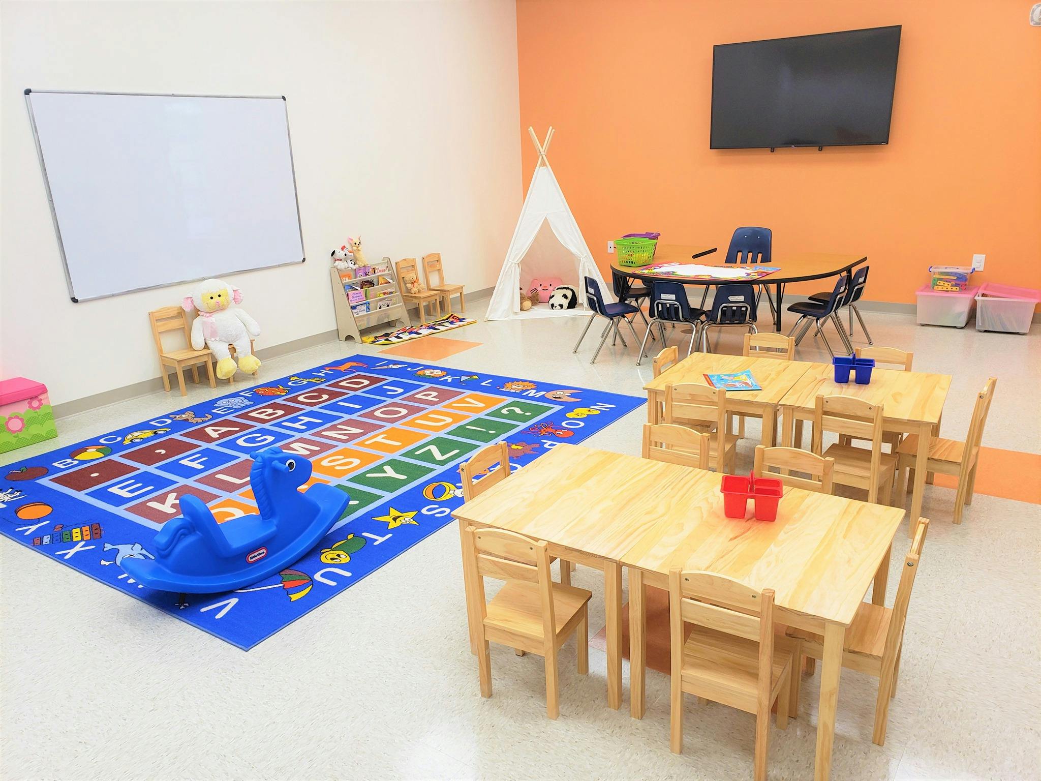 Classroom with small tables and chairs, alphabet rug, and whiteboard