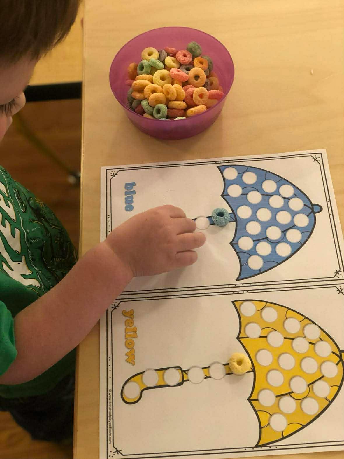 Child's hand placing a cereal piece on a learning sheet