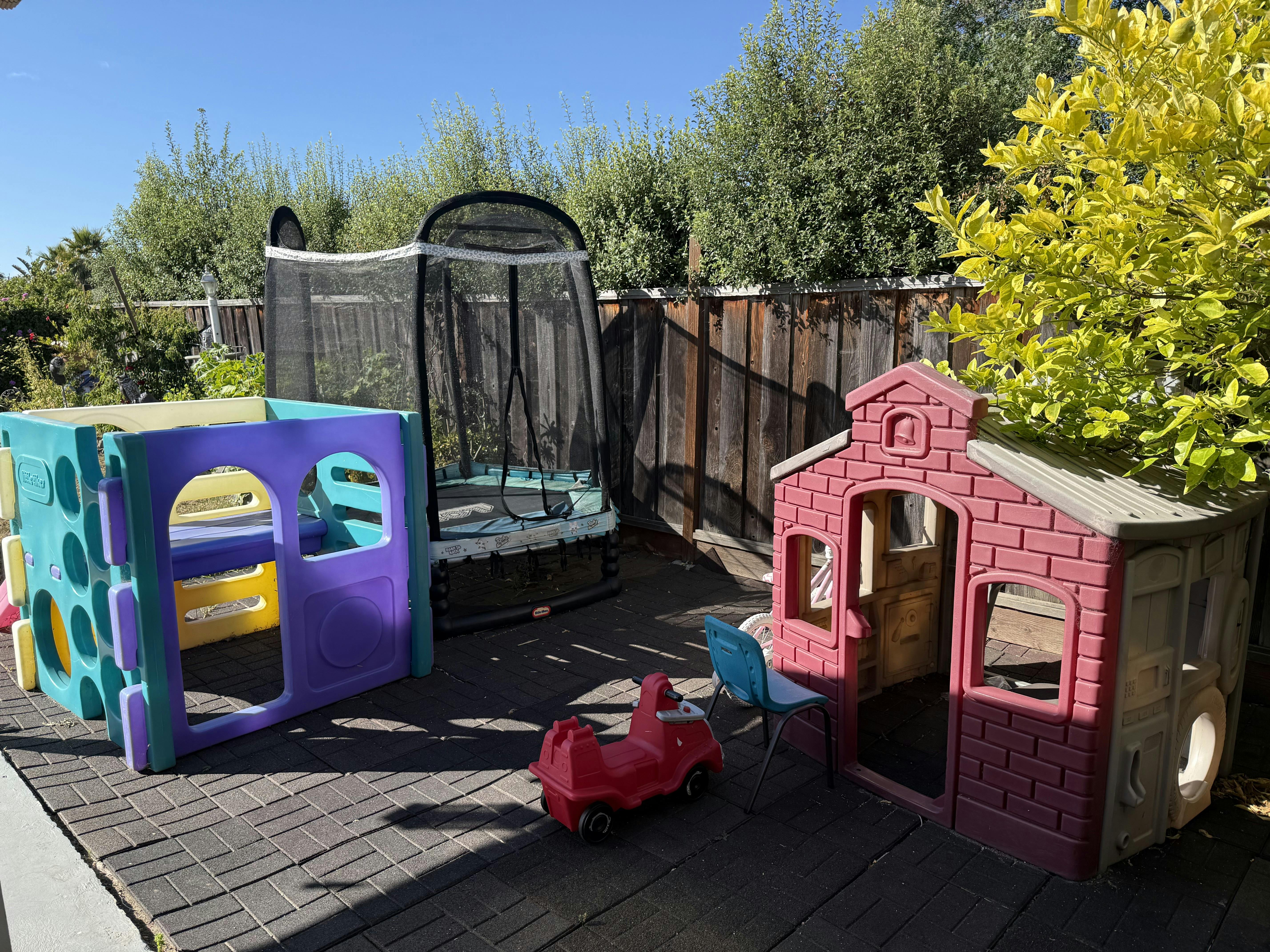 Playground equipment including a plastic playhouse and trampoline in a backyard
