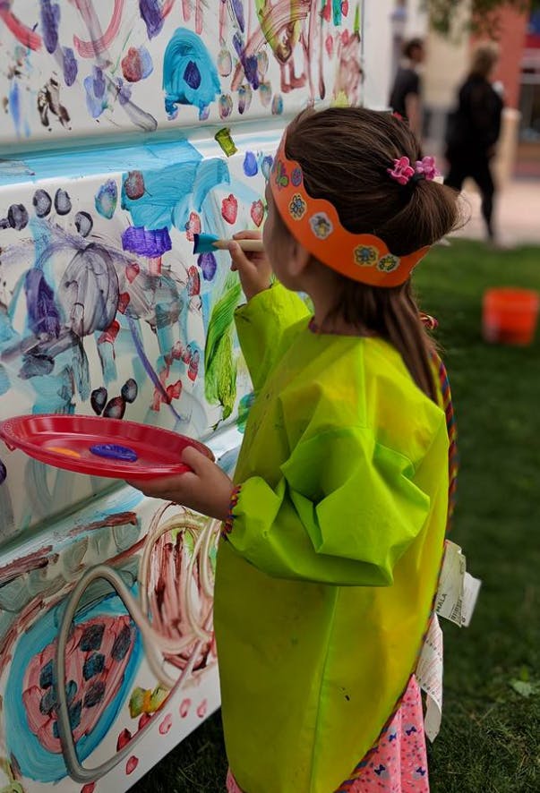 Child in a smock painting on a large canvas outdoors