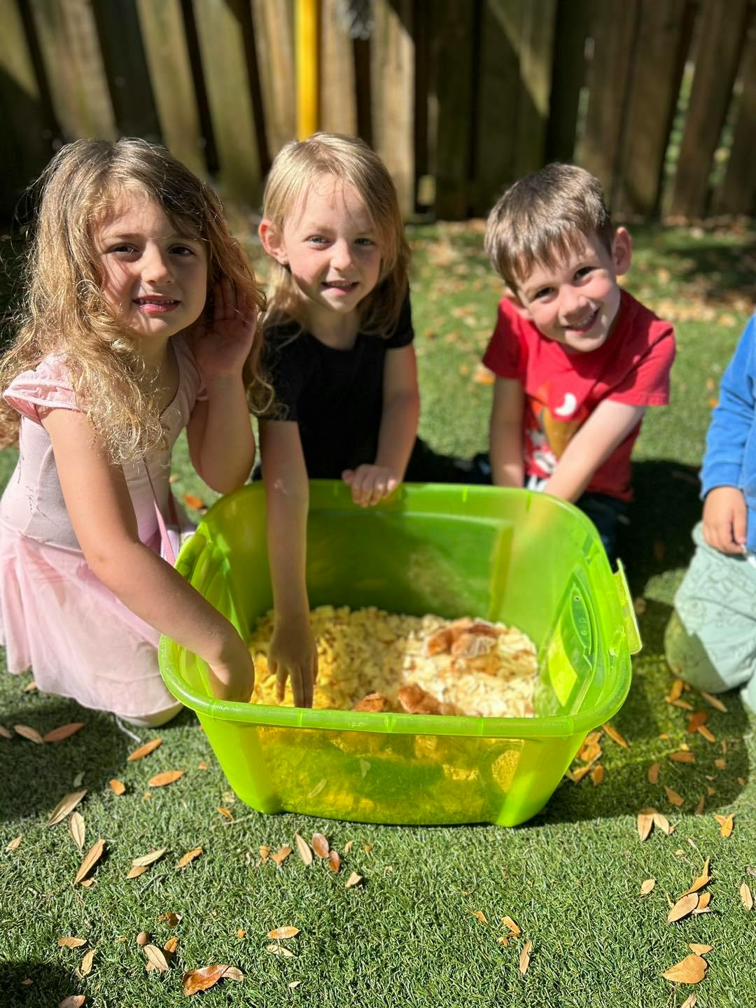 Three children playing with sensory bin outdoors