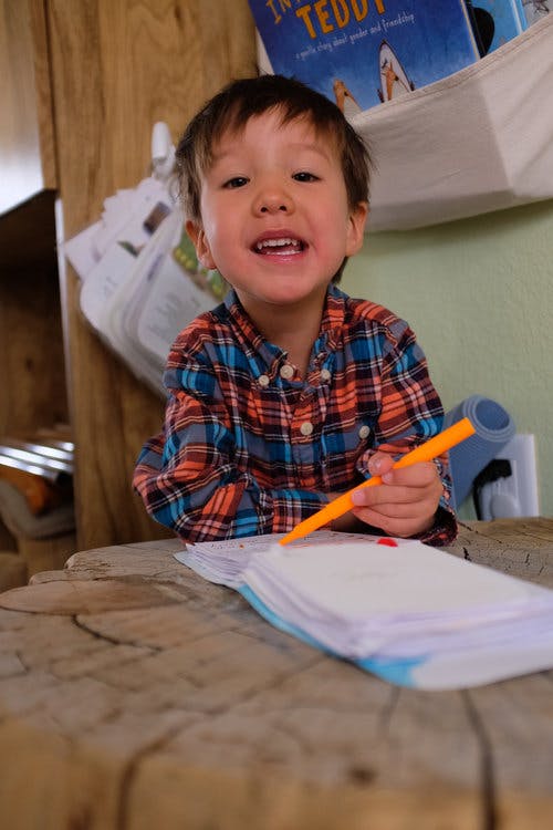 Child in plaid shirt holding an orange marker over paper