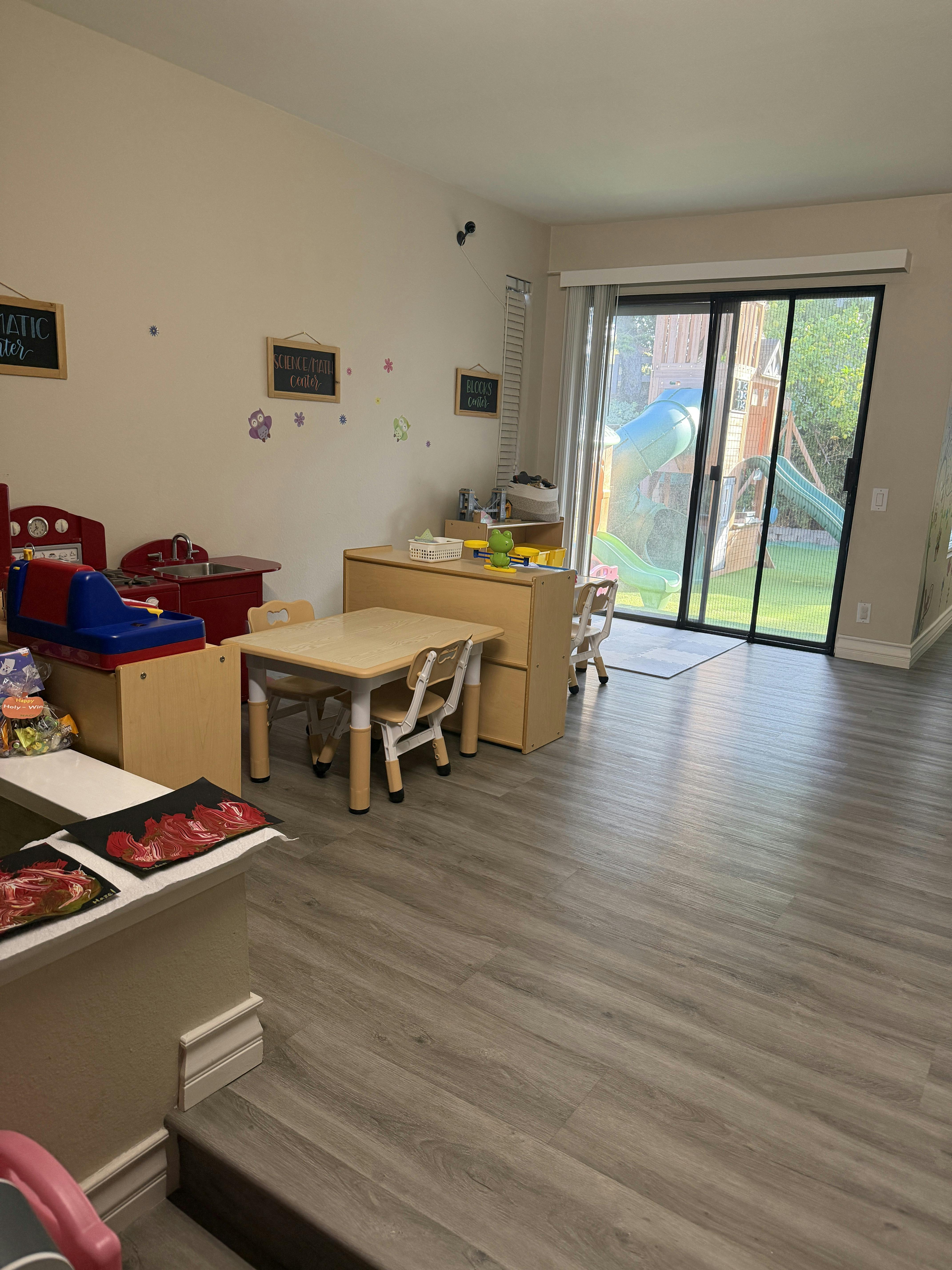 Children's play area with small table and chairs, toy kitchen, and sliding glass door