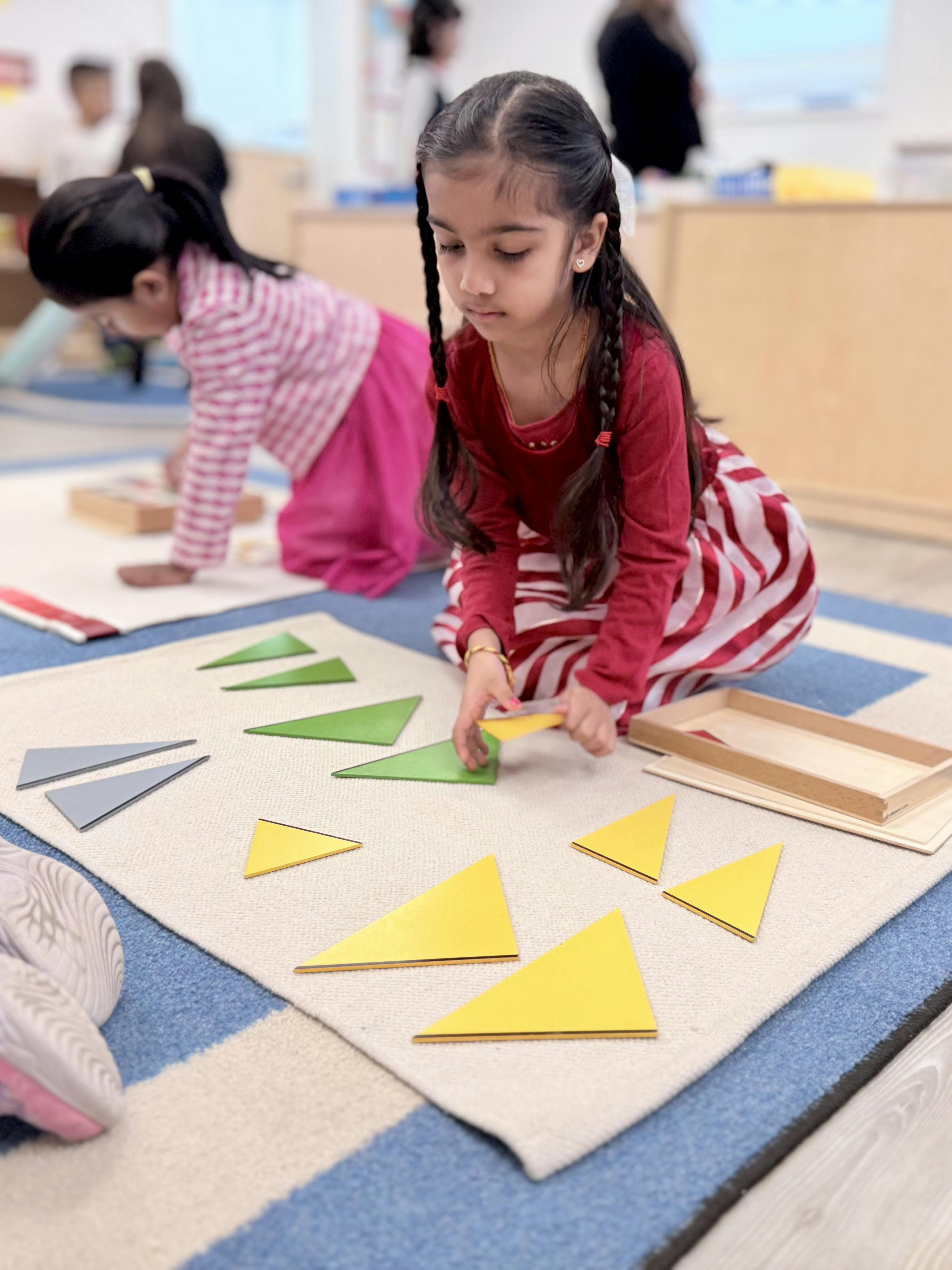 Child playing with triangle shapes on a mat, another child in the background