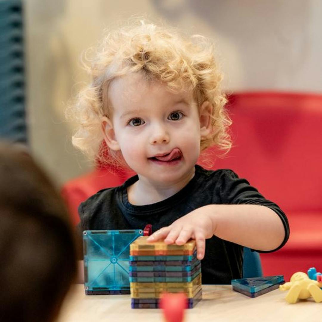Child with curly hair playing with colorful magnetic tiles