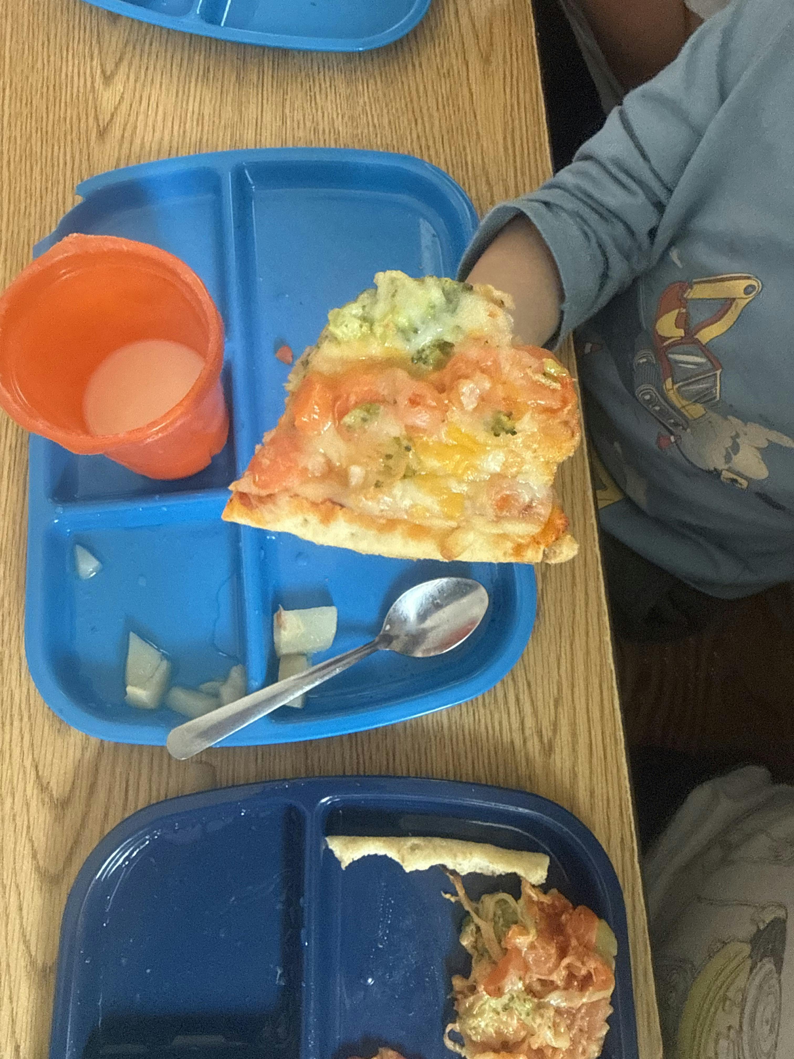 Child holding a slice of vegetable pizza over a blue partitioned tray