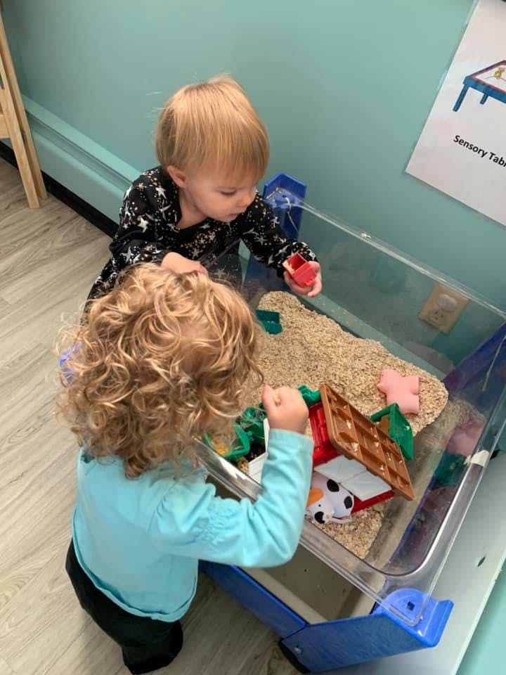 Two children playing with a sensory bin filled with sand and toys