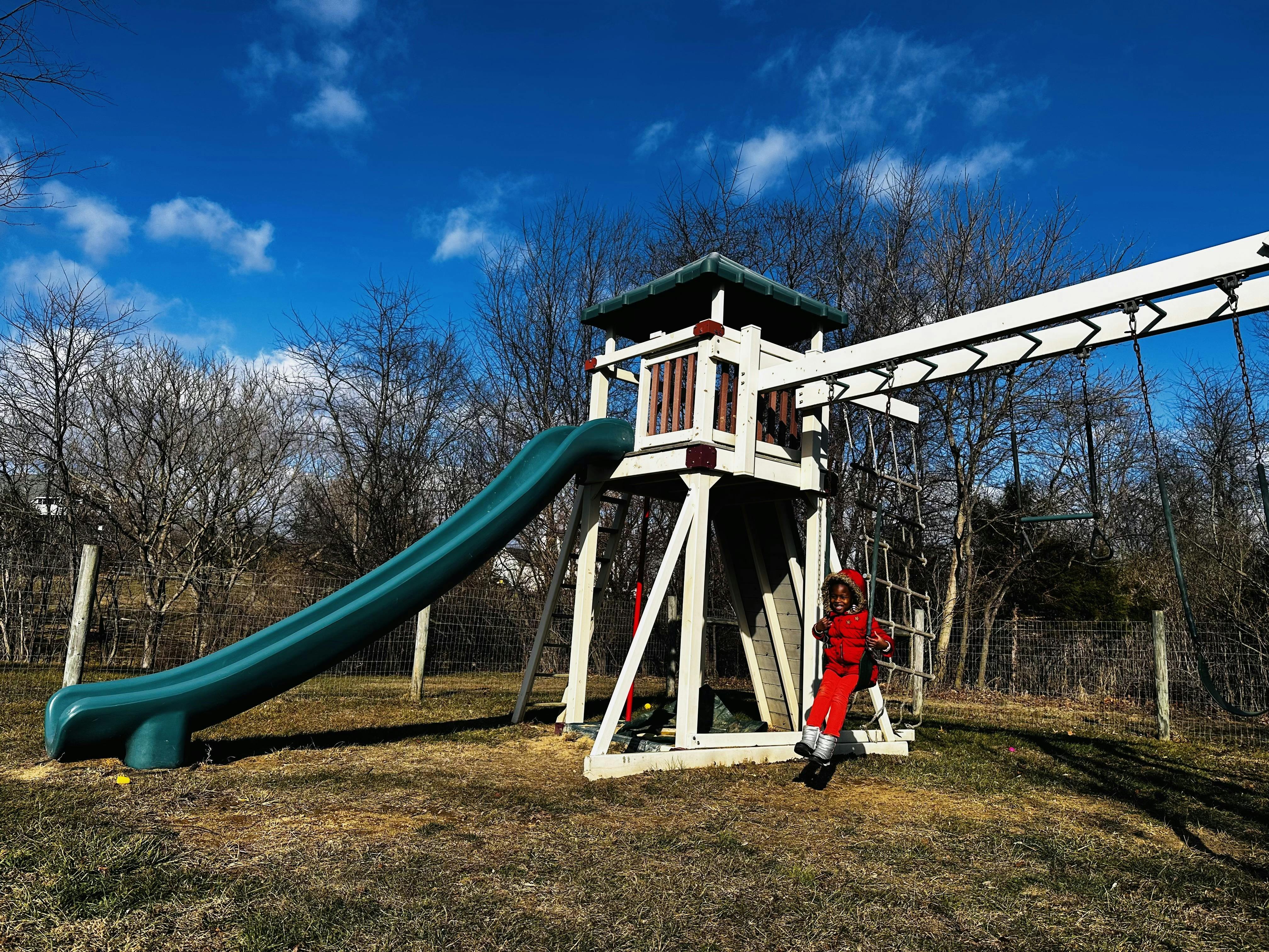 Child in red on a swing set with a slide