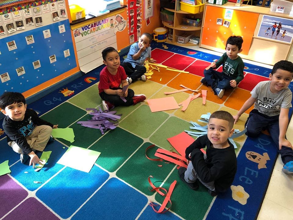 Children sitting on a colorful rug with paper and craft supplies