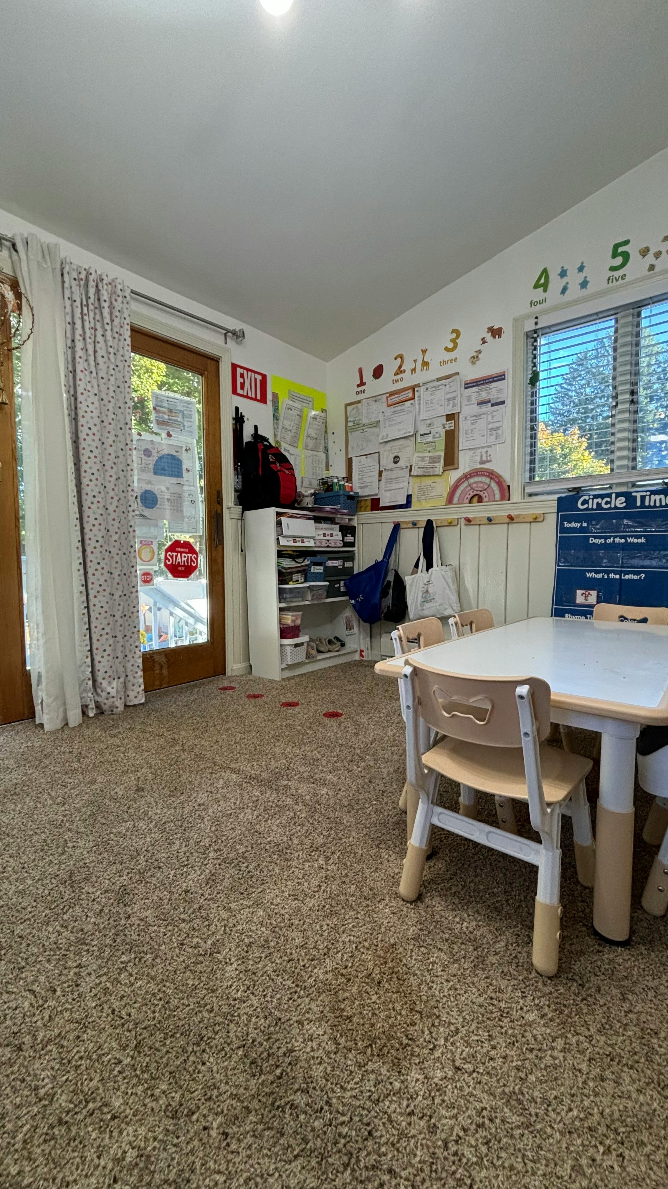 Classroom with small tables and chairs, bulletin board, and exit sign