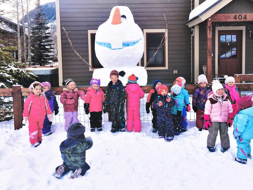 Children in winter clothing standing in snow with a large snowman decoration