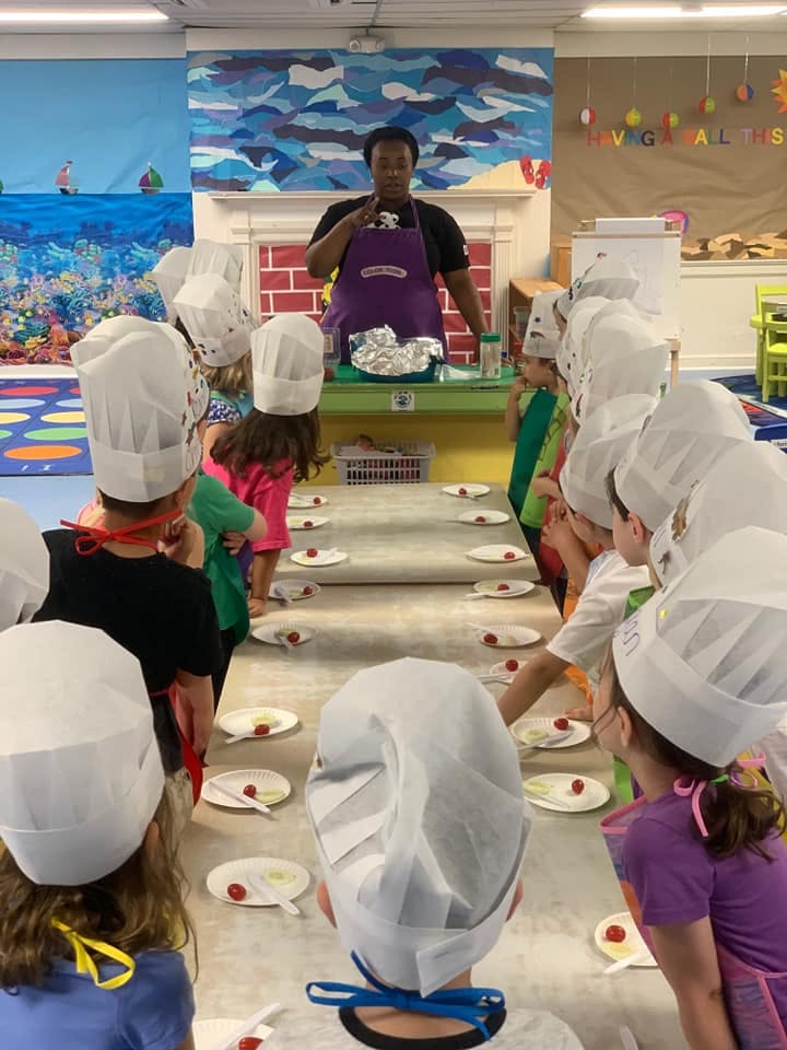 Adult leading a cooking class for children wearing chef hats