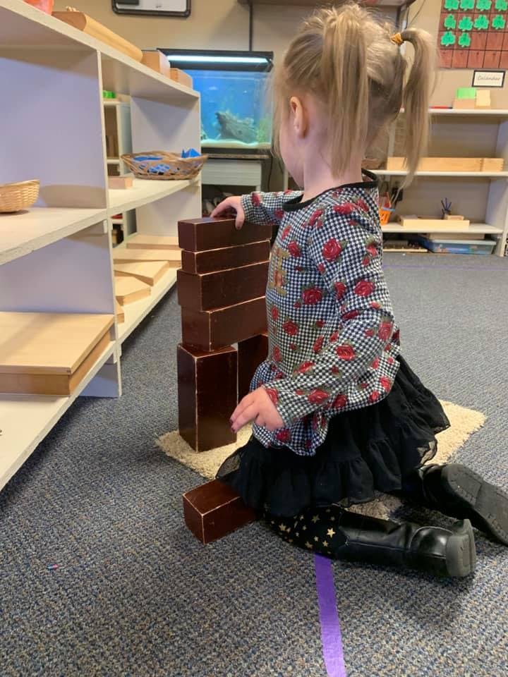 Child kneeling on floor building a tower with brown blocks