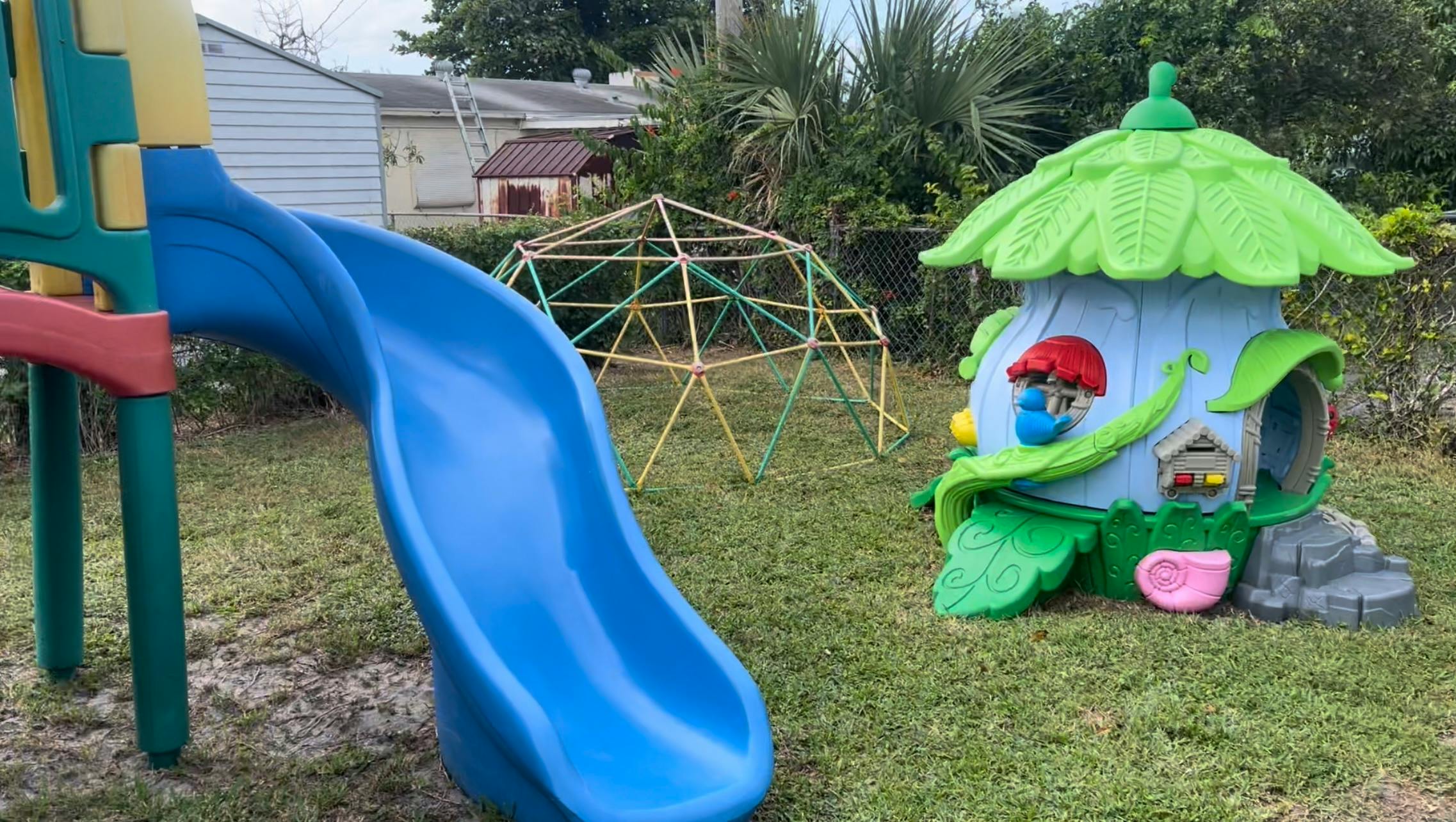 Playground with a blue slide, climbing dome, and a playhouse