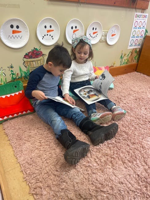 Two children sitting on a rug reading books