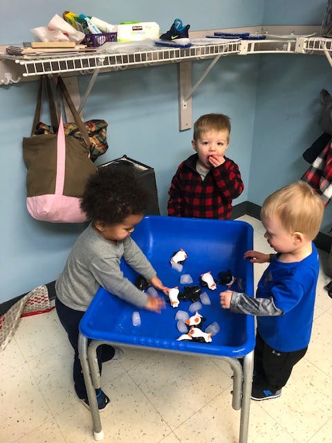 Three children playing with toys and ice in a blue bin