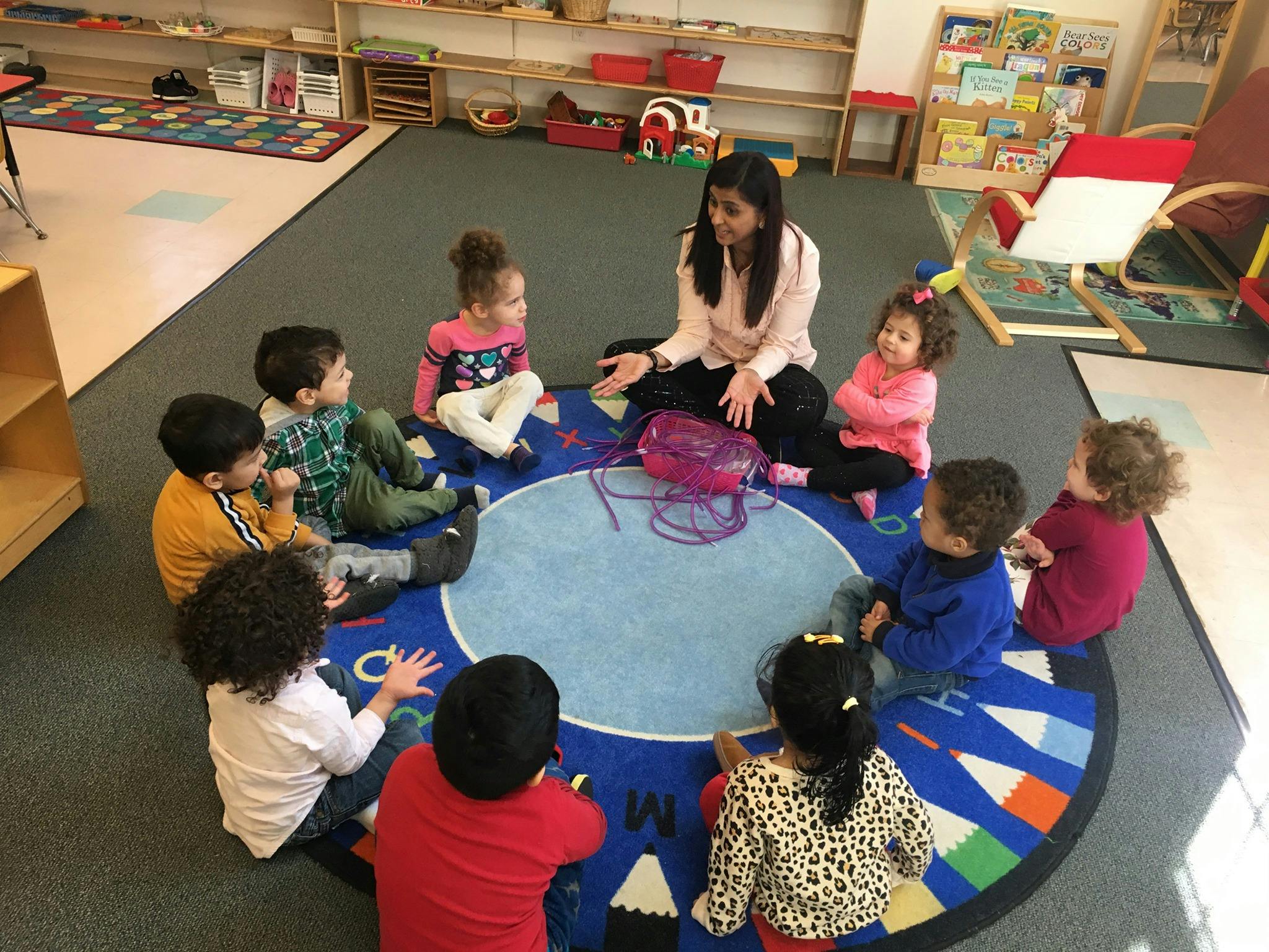 Adult and children sitting in a circle on a rug in a classroom