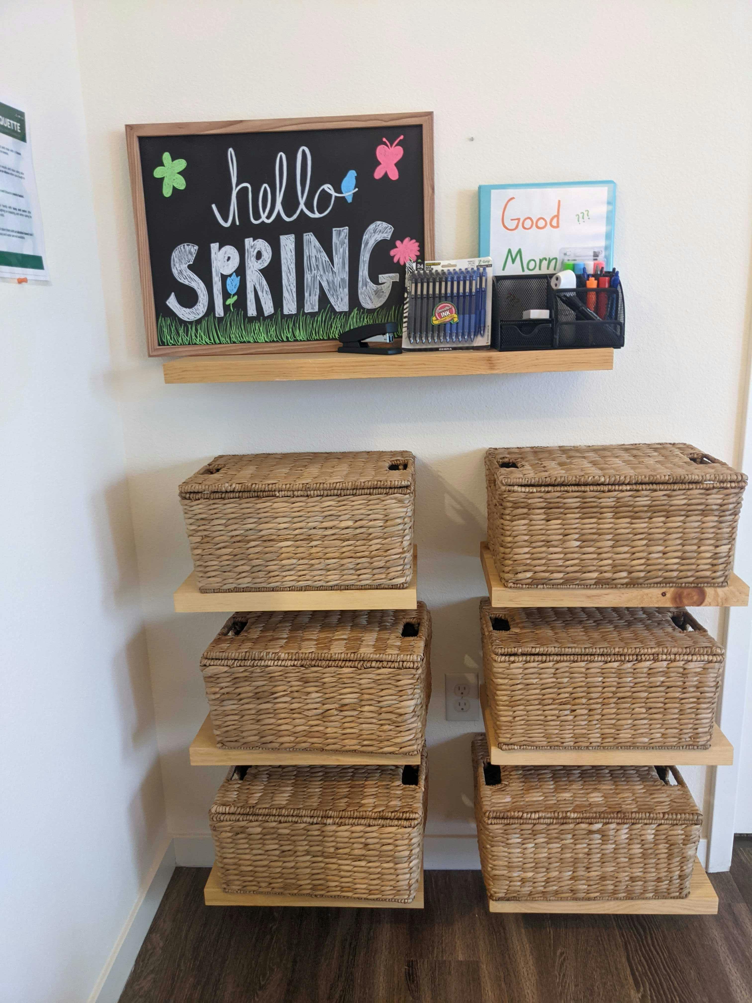 Chalkboard sign saying "hello SPRING" above wicker storage baskets
