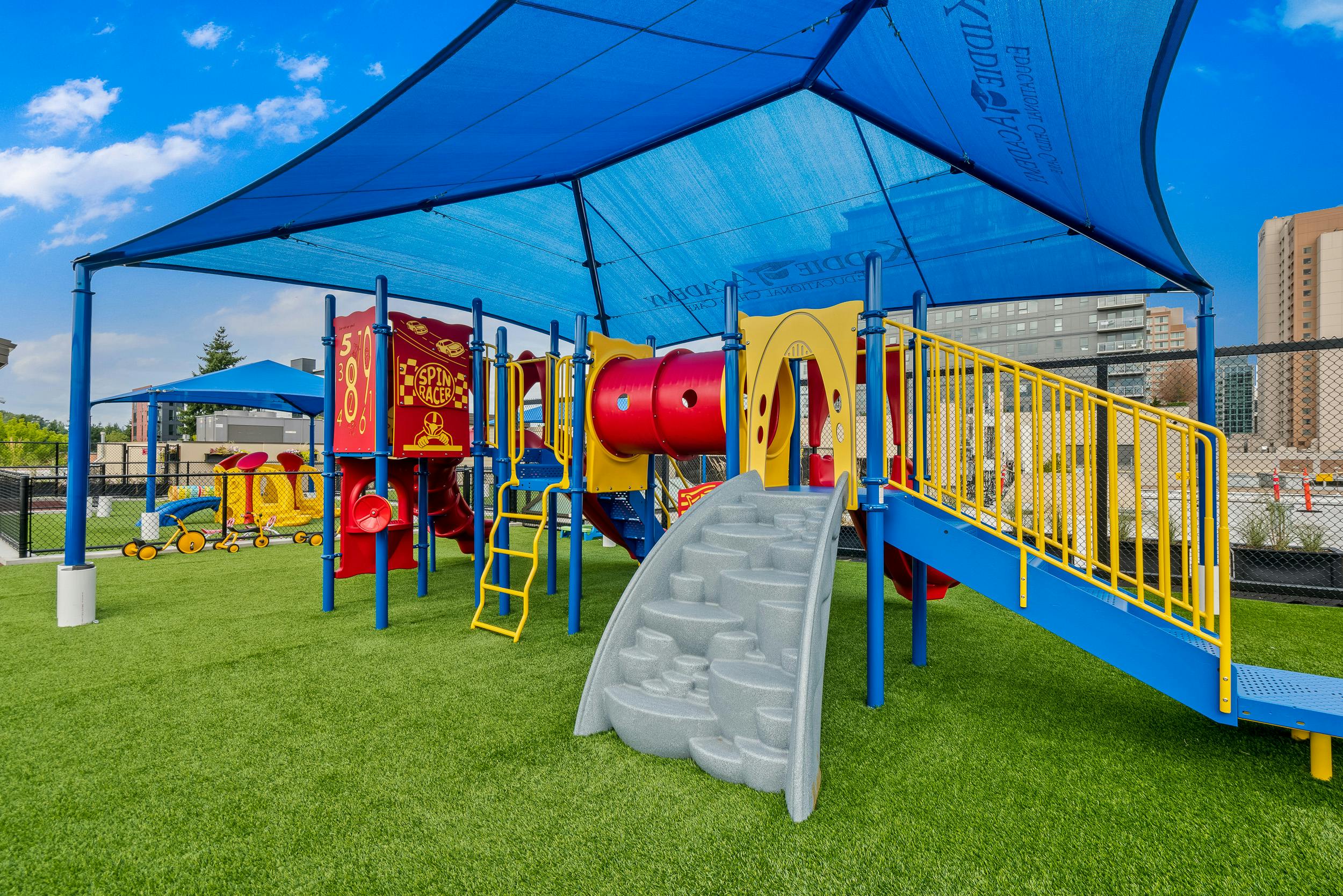 Playground with slides, tunnels, and climbing structures under a blue shade