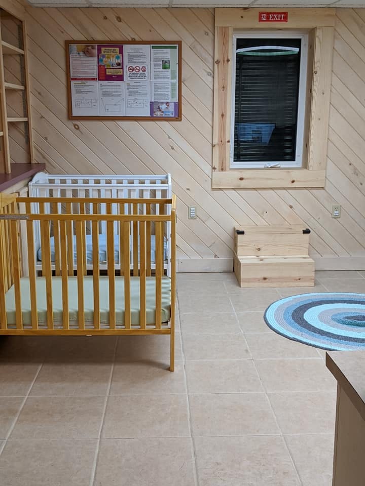 Two cribs in a room with wood paneling and a window
