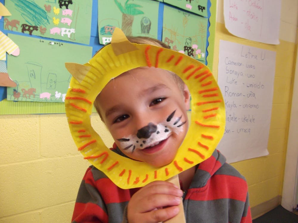 Child with face paint and a paper plate lion mask