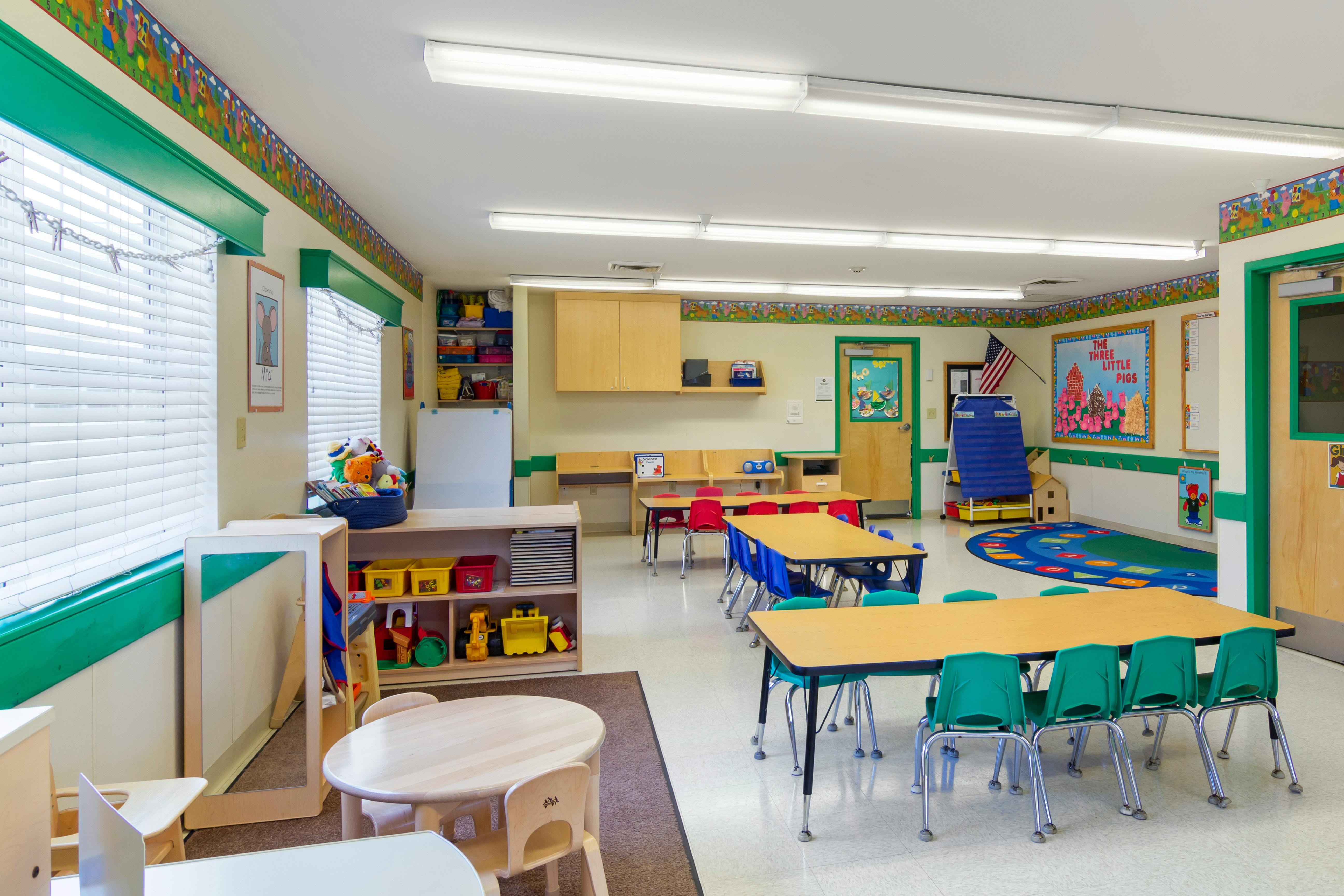 An empty classroom with several small tables and chairs, toys, and learning materials