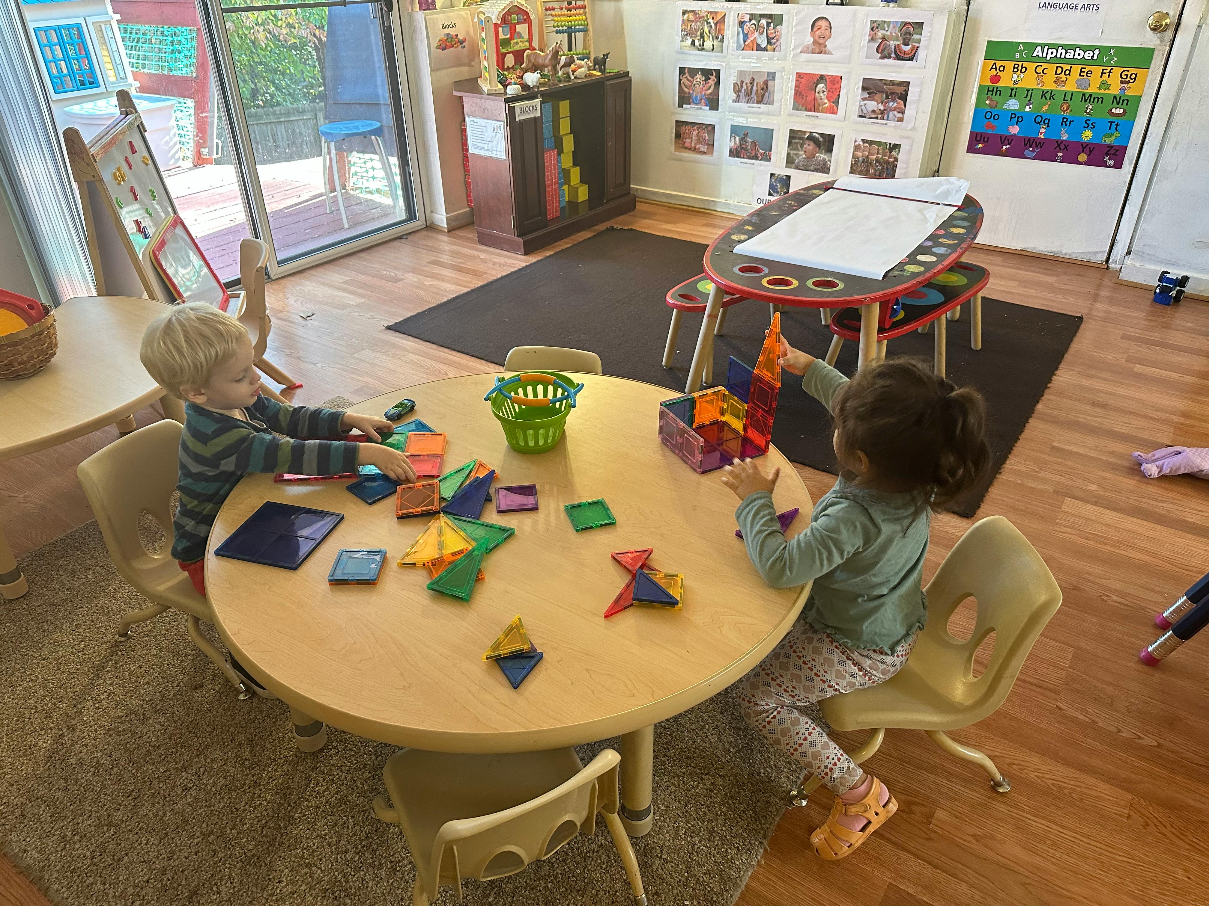 Two children playing with magnetic tiles at a table in a classroom