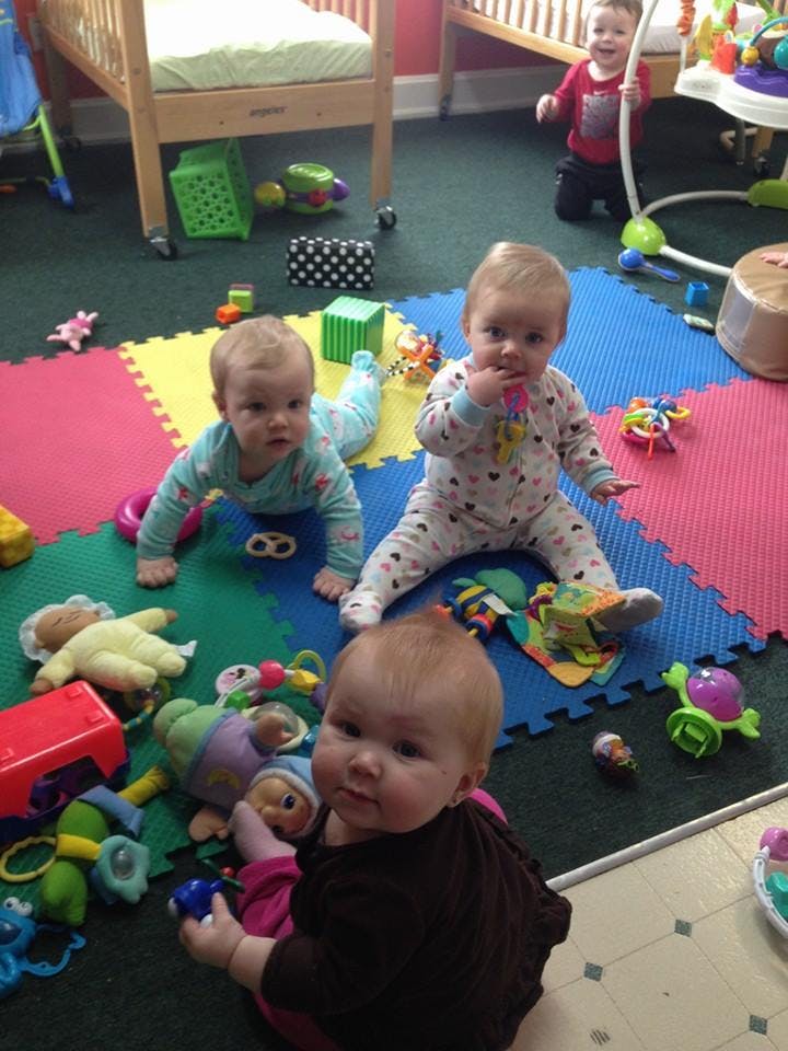 Multiple babies playing on a colorful mat with toys