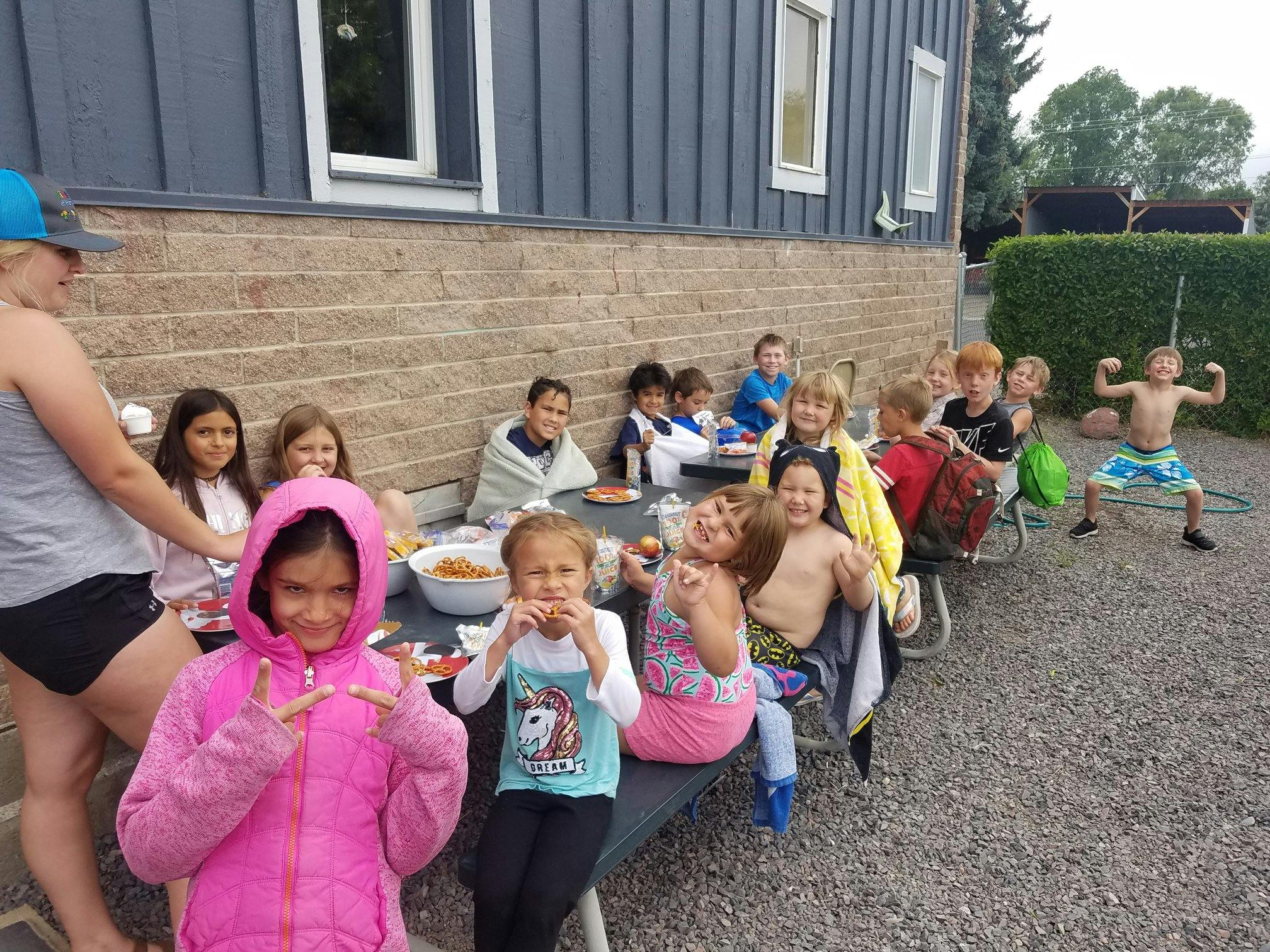 Group of children and teens eating at an outdoor table