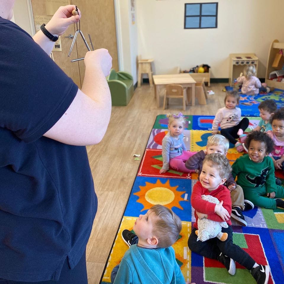 Person holding a triangle instrument for a group of children in a classroom