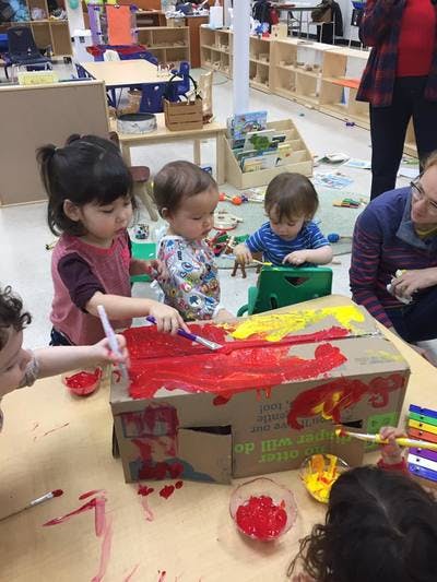 Children painting a cardboard box with red and yellow paint