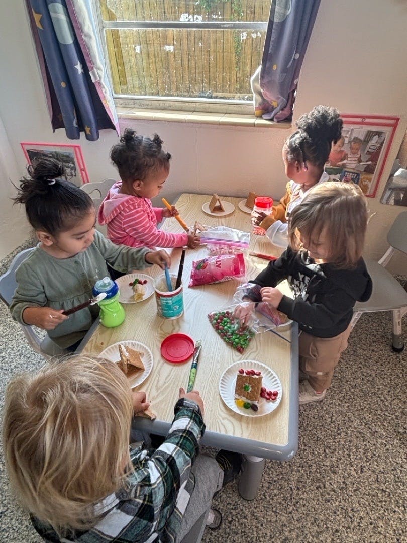 Children decorating gingerbread houses at a table in a classroom