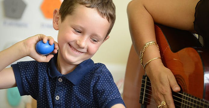 Child holding a blue egg shaker next to a person playing guitar