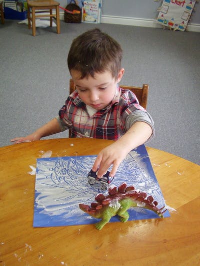 Child playing with toy car and dinosaur on a table