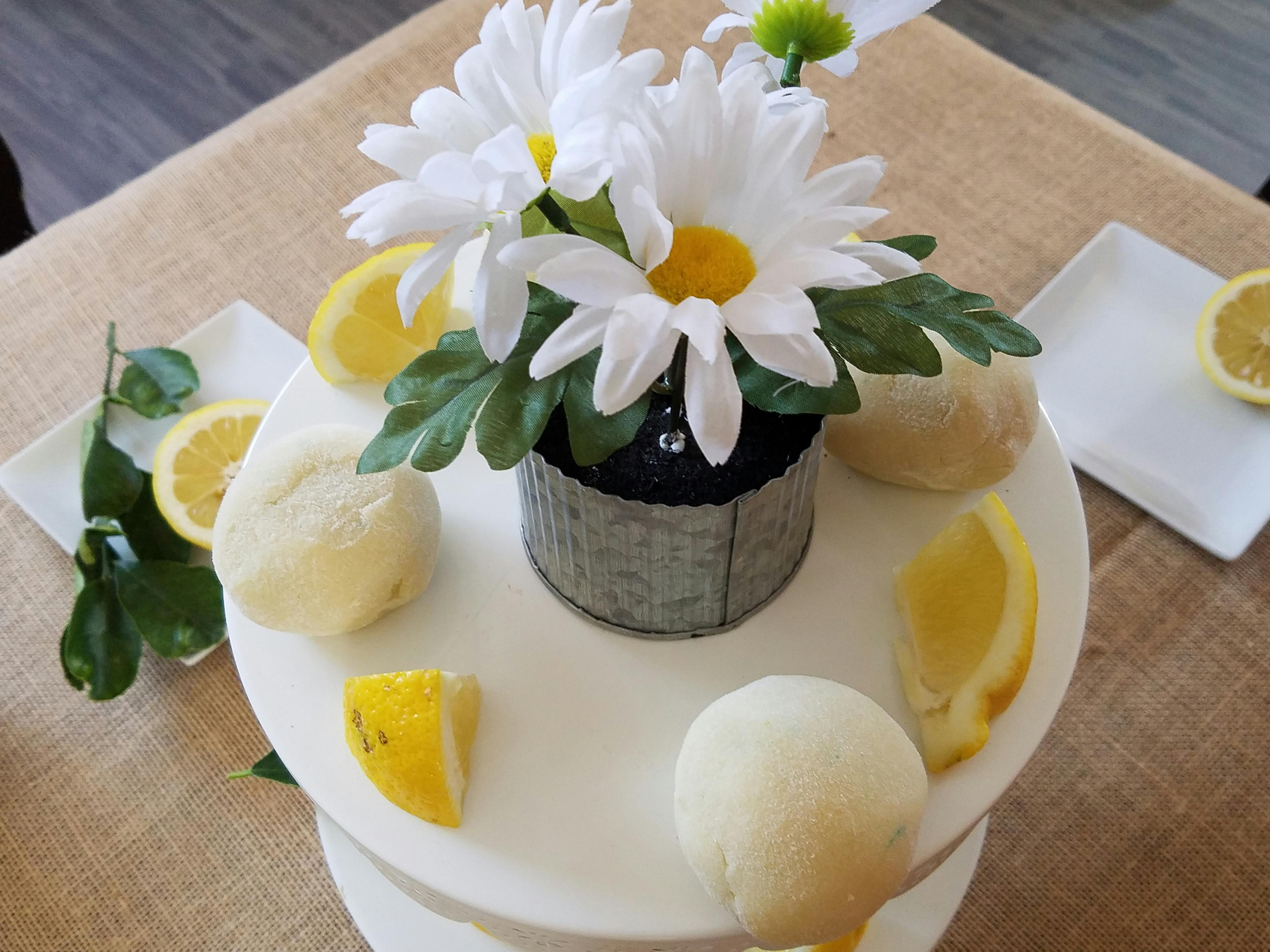 White daisies in a pot with lemons and lemon-shaped desserts on a tiered stand
